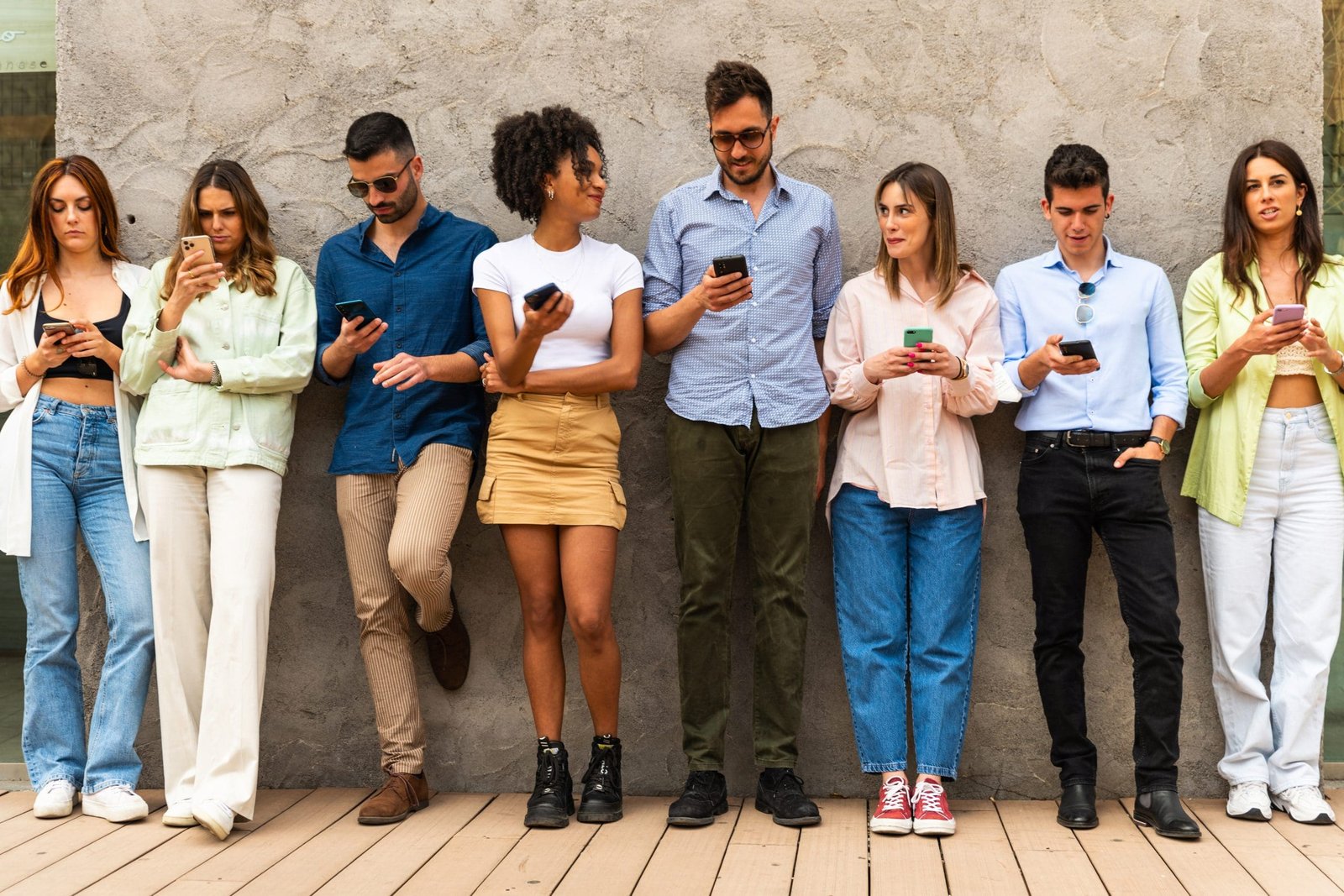 Multiracial friends using smartphone against wall at university college backyard